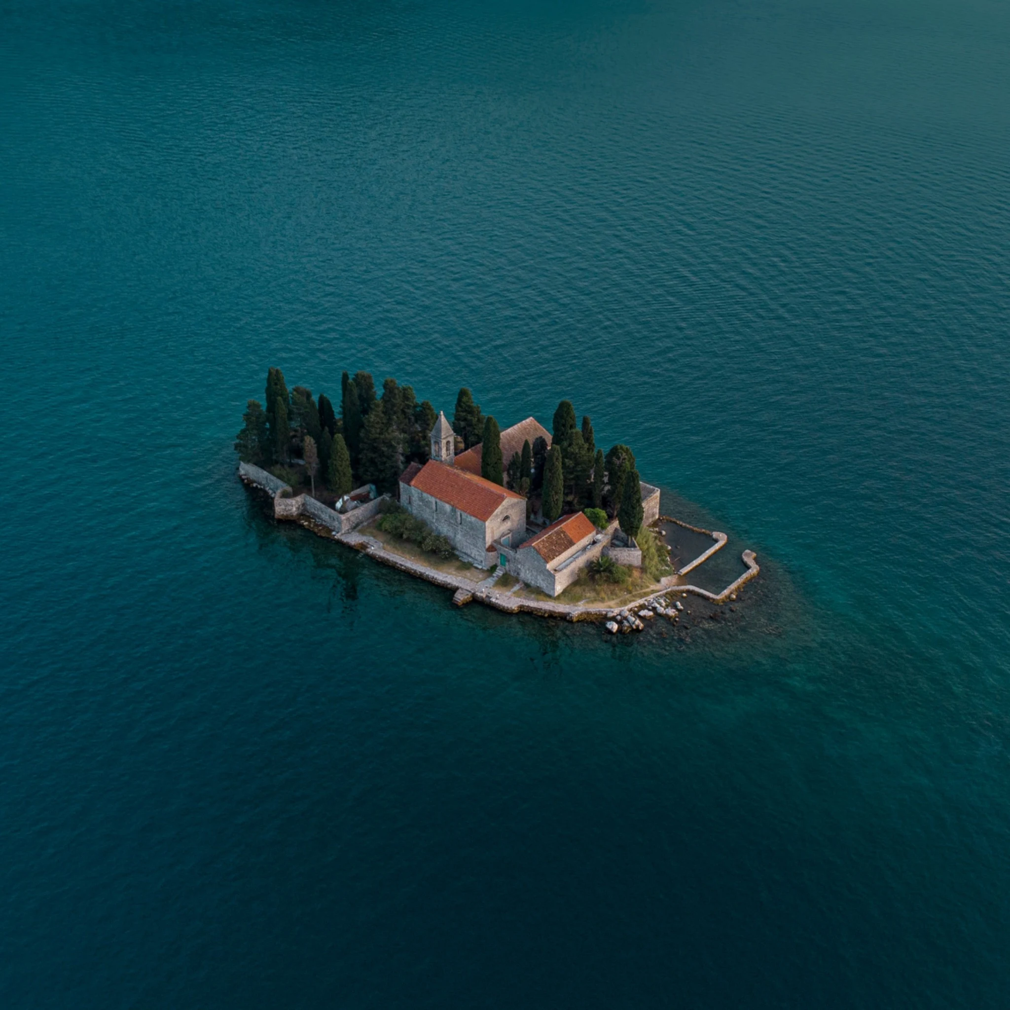 A small island with stone buildings and cypress trees surrounded by turquoise water