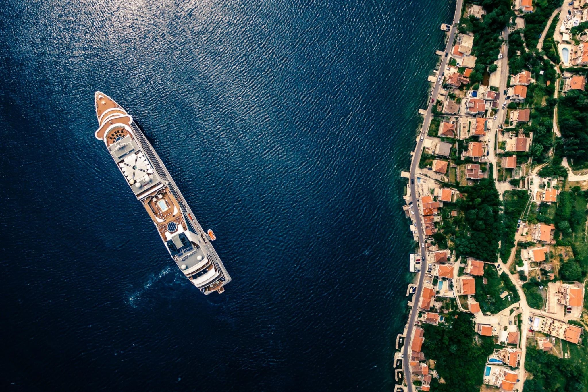 Aerial view of a yacht on deep blue water beside the Bay of Kotor waterfront